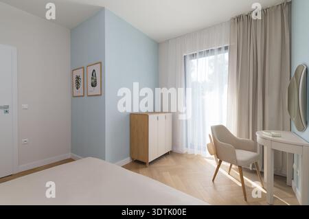 Modern bedroom interior design featuring a light blue accent wall and herringbone parquet flooring. The room includes a white dressing table with a be Stock Photo