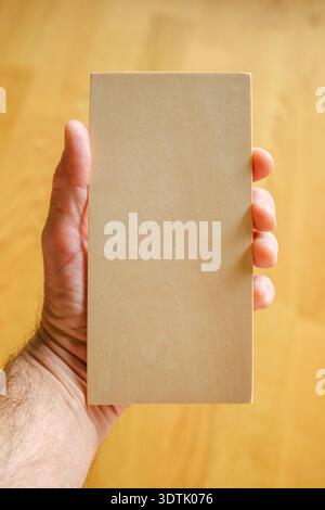 Person holding small rectangular wooden plate template, minimal object for branding or engraving design. Selective focus. Stock Photo