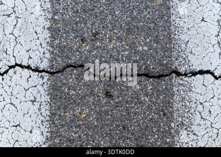 Cracked asphalt road surface with white road marking, close-up texture, top view Stock Photo