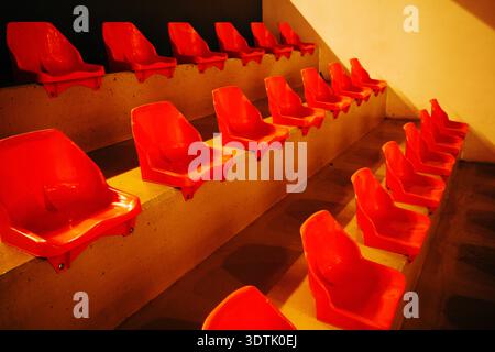 Empty red arena chairs aligned in rows with strong symmetry and vivid color contrast, abstract seating pattern in indoor sports venue. Selective focus Stock Photo