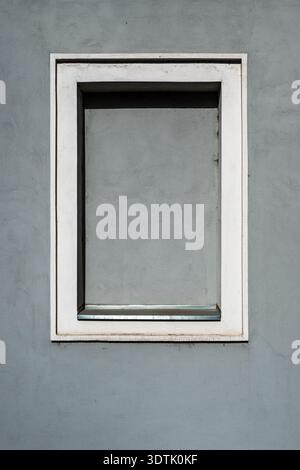 Small square window with white frame set in smooth gray plaster wall, minimalist architectural detail with clean geometry and subtle texture. Vertical Stock Photo
