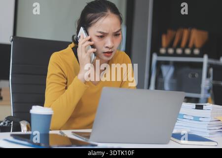 Young professional woman suffering from headache while analyzing financial charts and graphs on computer, experiencing work related stress in modern o Stock Photo