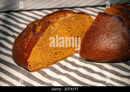 A beautifully baked rye bread loaf sliced in half placed on a black and white striped cloth. The rich brown crust contrasts with the soft, dense inter Stock Photo