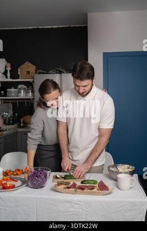 A couple is joyfully preparing a healthy meal together in their modern kitchen. The table is laid with fresh vegetables and meats, creating a vibrant, Stock Photo