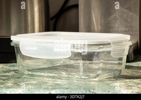 A glass container with a plastic lid on a kitchen countertop for storing food, carrying lunch, sealing leftovers, and protecting food from air Stock Photo