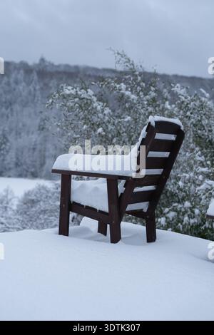 Single wooden chair standing in deep fresh snow against open winter landscape. Minimal composition emphasizing solitude, silence and vast natural Stock Photo