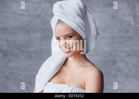 Woman With Towel on Head Smiles After Shower in a Bathroom With Gray Background Stock Photo