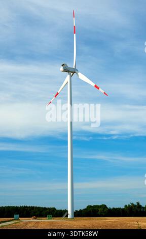 A striking white Vestas wind turbine with three blades, each featuring a red tip, stands tall against a bright blue sky dotted with wispy white clouds Stock Photo