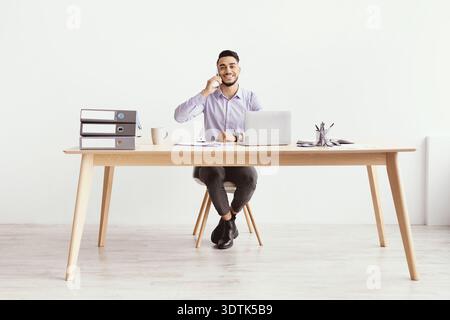 Business Professional Talks on the Phone While Seated at Desk in Light Workspace Stock Photo