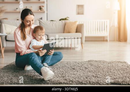 Happy mother and her kid son using digital tablet at home, watching development videos or surfing internet, copy space Stock Photo