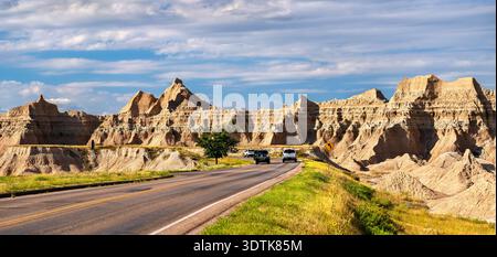 Cars driving along a scenic paved road winding through the rugged rock formations at Badlands National Park, South Dakota, United States Stock Photo