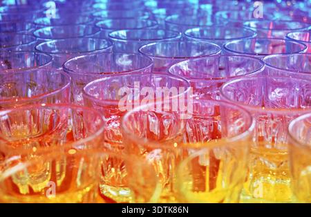 A close-up, high-angle view of numerous empty glass tumblers arranged in rows. The lighting creates a vibrant color gradient across the image, transit Stock Photo