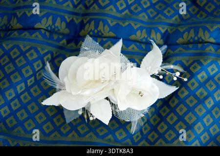 A close-up shot of a decorative white floral accessory, likely a hair clip or corsage, resting on a textured dark blue fabric. The accessory features Stock Photo