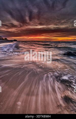 A breathtaking long exposure photograph captures a dramatic coastal sunset. The sky bursts with vibrant hues of orange and red along the horizon, grad Stock Photo