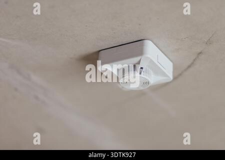 White Smoke Detector Installed On Concrete Ceiling. Fire Safety Device In Unfinished Interior. Stock Photo