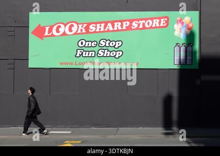 Pedestrian walks beneath Look Sharp Store billboard in Wellington, New Zealand. Stock Photo