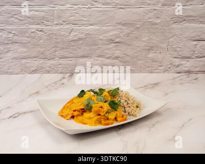 Gourmet prawn coconut curry with brown rice on a marble surface against a white brick wall background. Stock Photo