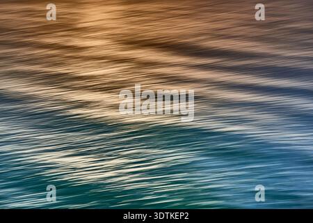 A captivating abstract image of a water surface featuring a smooth color gradient from warm orange-brown tones at the top to cool blue-green hues at t Stock Photo