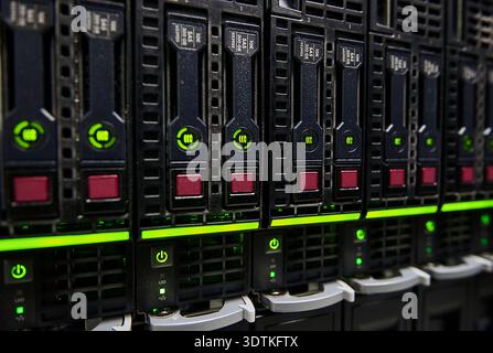 A close-up, eye-level shot of a server rack populated with multiple hard drive bays. The drives are black, each featuring a prominent green illuminate Stock Photo