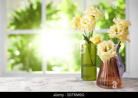 Eustoma flowers in vases on table against window. Beautiful composition Stock Photo
