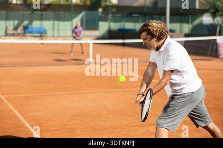 Handsome athletic man serving with racket in hands while practicing on tennis court in day Stock Photo