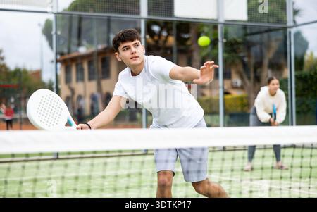 Sportive young man holding padel racquet in hand and ready to return ball while playing in court Stock Photo