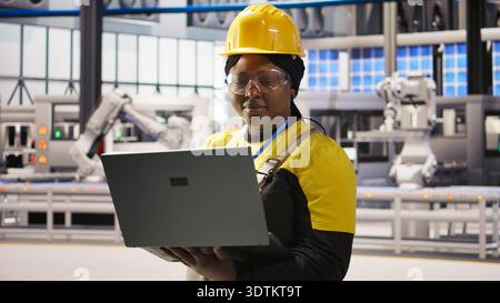Solar panels factory engineer analyzing data from IoT sensors to refine equipment operational efficiency. Worker performing system diagnostics to reduce downtime in photovoltaic production, camera A Stock Photo