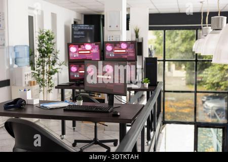 Desktop monitors show system error warnings in empty office workspace. The scene represents software failure, technical issues and business interruption in modern IT environment. Stock Photo