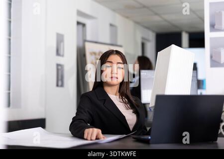 Female architectural designer reviewing blueprints and researching building concepts. Woman architect focuses on planning tasks, organizing timelines and preparing reports for company projects. Stock Photo