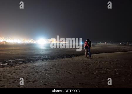 A young couple shares an intimate embrace on Matalascañas Beach, Almonte, Huelva, Spain, under the night sky during a warm summer evening. Stock Photo