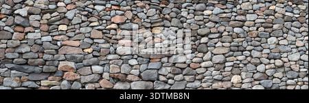 Rock wall made of small rocks on concerete background. Background image. Panorama horizontal image. Background texture Stock Photo