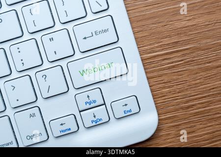 A computer keyboard on a wooden desk with a green Webinar key. Online education, virtual seminars, remote work concept. Copy space for text. Stock Photo