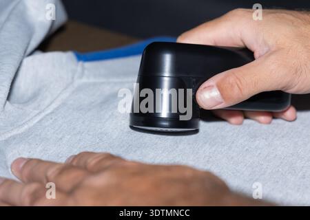 A person is using a handheld steamer to remove wrinkles from a gray sweatshirt on a flat surface. Stock Photo