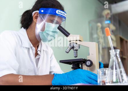 African american Scientist man look into Microscope research in science laboratory. Asian biochemistry scientist using microscope in laboratory chemis Stock Photo