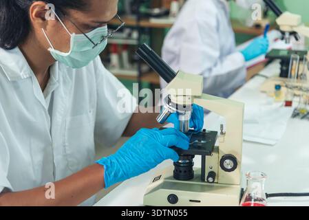 African american Scientist man look into Microscope research in science laboratory. Asian biochemistry scientist using microscope in laboratory chemis Stock Photo