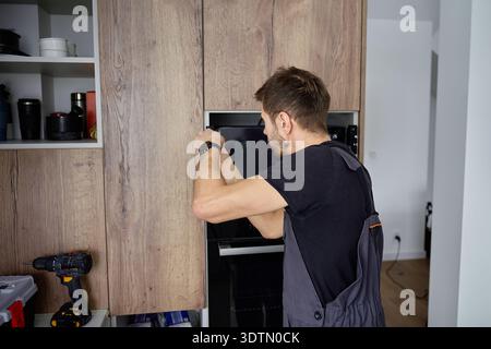 Man using screwdriver to fixing new built in microwave oven with screws in modern kitchen cabinet. Concept of home appliances installing Stock Photo