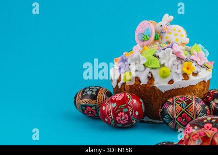 A cake is displayed with various decorations for Easter. Around the cake are several painted eggs in bright colors. The setting has a blue background. Stock Photo