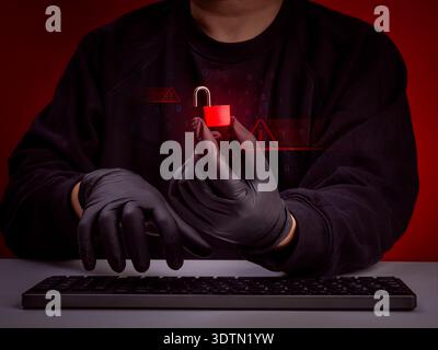 Cyber security concept with anonymous hacker holding red unlocked padlock and digital warning symbols. Data breach, hacking attack, information theft, Stock Photo