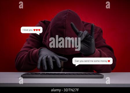 Hacker in hoodie and gloves using online romance scam tactics, sending fake love messages to deceive victims for money with I love You hand sign. Cybe Stock Photo