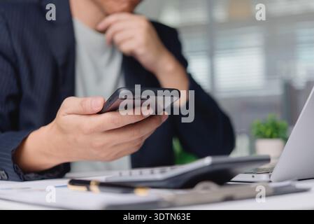 Businessman thinking, analyzing financial data on smartphone at office desk. Man using mobile app for investment planning, stock market research. Busi Stock Photo