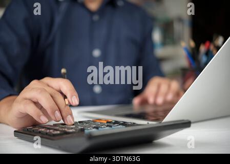 Businessman hand using calculator, laptop for financial analysis, tax calculation. Man working on accounting report, budget planning on office desk. B Stock Photo