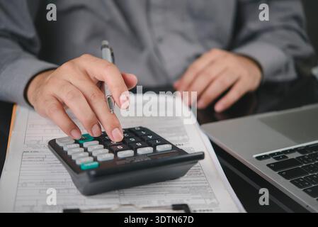 Man hand using calculator for financial analysis, tax calculation. Businessman working on accounting report with document, laptop on office desk. Busi Stock Photo