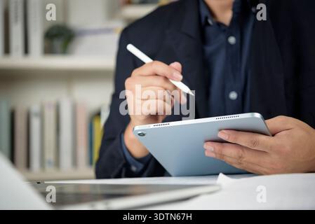 Close up professional man working on tablet with pen. Executive signing digital document, taking notes during online meeting. Multitasking, productivi Stock Photo