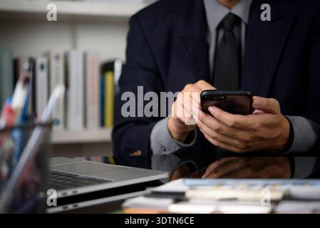 Man hands holding smartphone, working in modern office. Executive manager checking email, scheduling meetings on mobile app. Multitasking with laptop Stock Photo