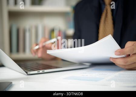 Businessman hand holding document, reviewing financial report with laptop at office desk. Manager analyzing paperwork, contract for business audit. Co Stock Photo