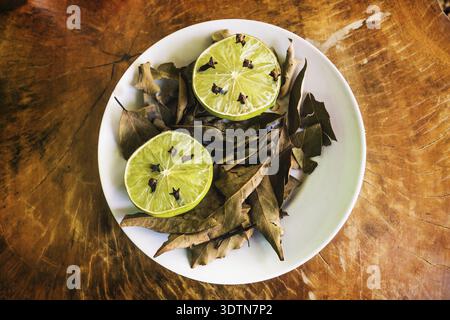 Natural repellent white plate with fresh lime, cloves and dried laurel on wooden table Stock Photo