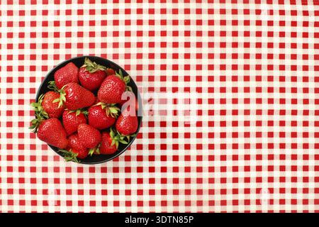 Tabletop view, small black ceramic bowl of strawberries on red chequered gingham tablecloth, Liptovsky Hradok, Slovakia Stock Photo