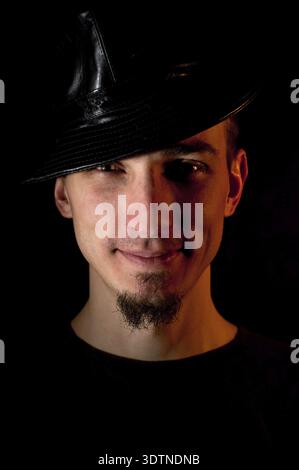 Studio portrait of smiling handsome man in hat over black background. Low key image red lighting used Stock Photo