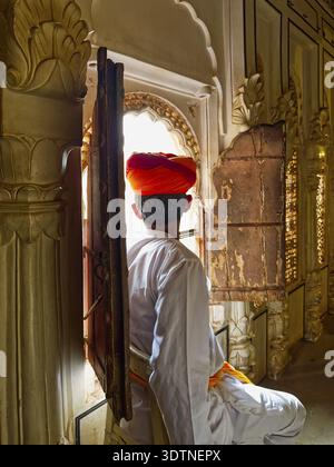 Rear view of an Indian man in traditional clothes looking out the window of the old house Stock Photo