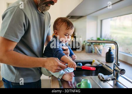 Father caring for toddler son while doing household chores. Stock Photo